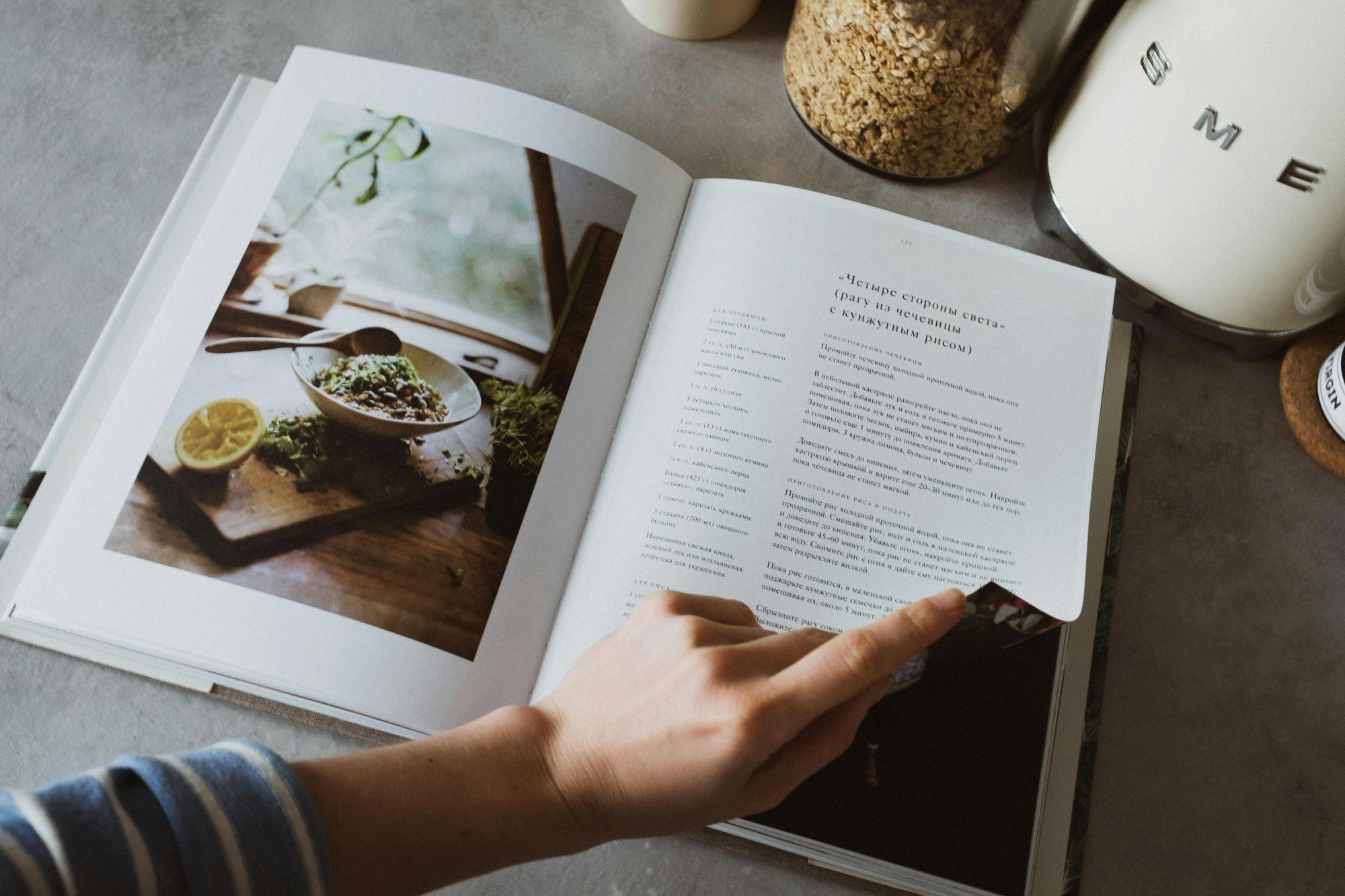 Person paging through a recipe book in a kitchen with small appliances on the table
